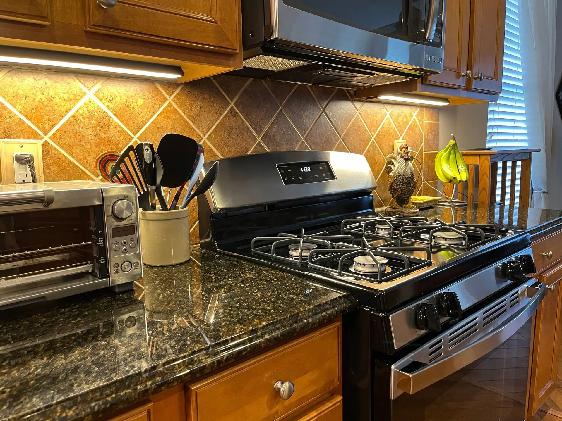 A kitchen counter with a toaster oven, a utensil crock, a gas stove, and tiled backsplash under wooden cabinets.