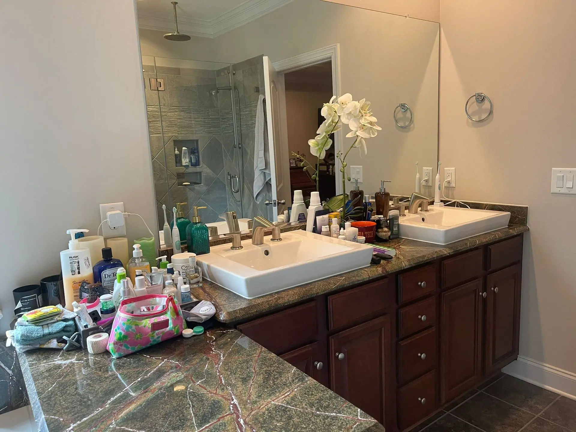 A double-sink bathroom vanity with dark wood cabinets, granite countertops, and many personal care items on the counter.