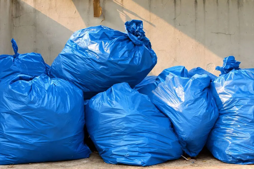 Blue garbage bags piled against a concrete wall.